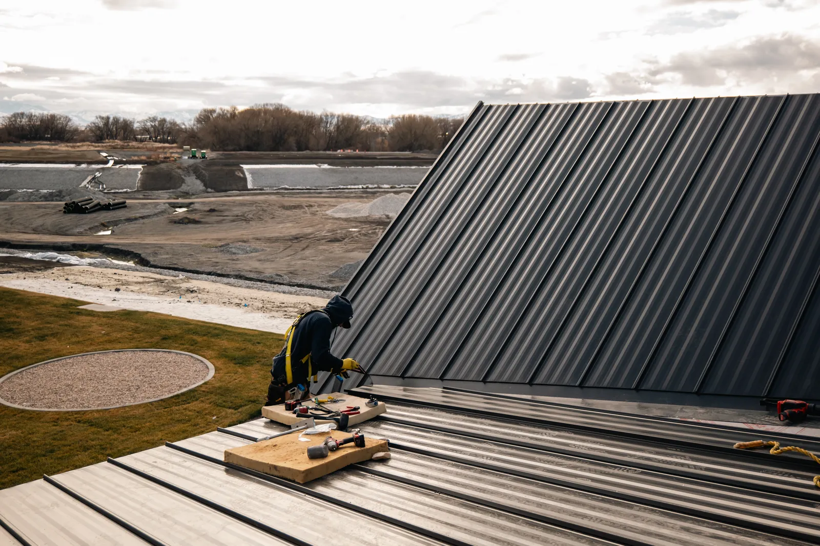 Charcoal standing seam metal roof being installed on a steep-pitch new construction home in Northern Utah