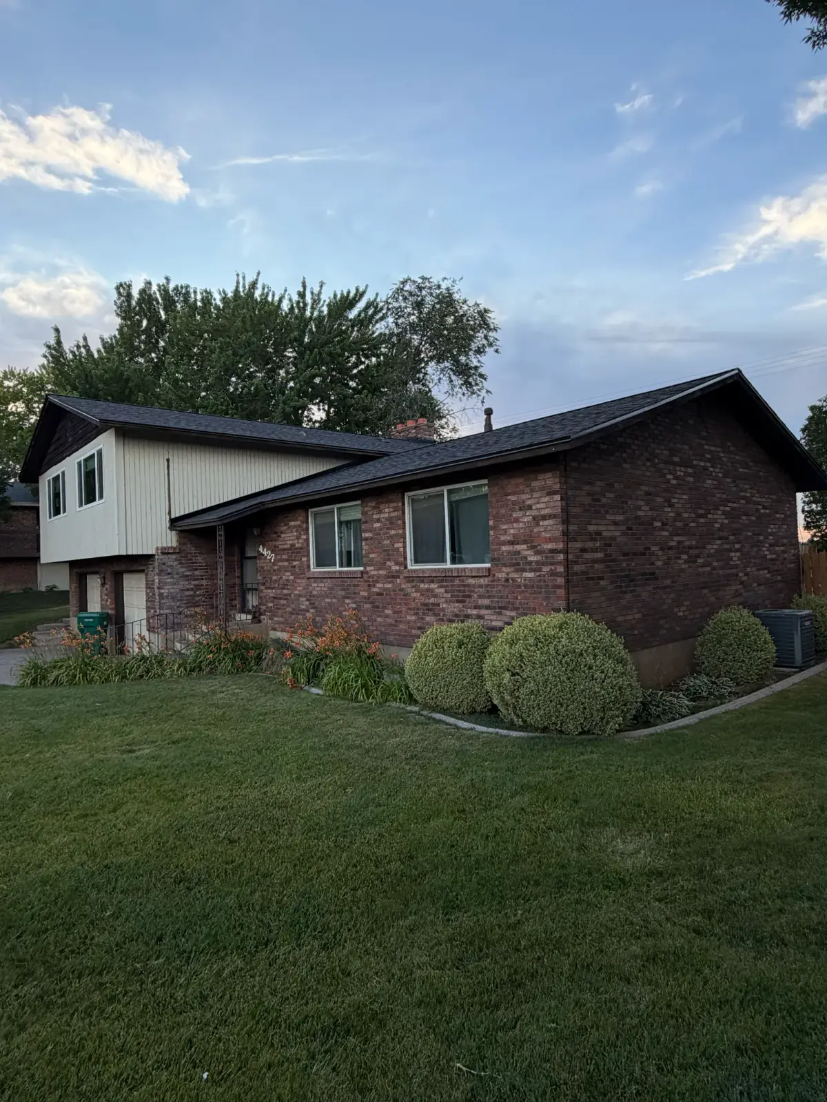 Front view of a Roy, Utah brick home with a new charcoal asphalt shingle roof installed by Homer Roofing